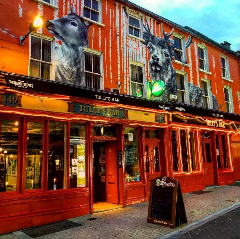 Tully's Bar at dusk, the red shopfront lit up under the grey stag murals